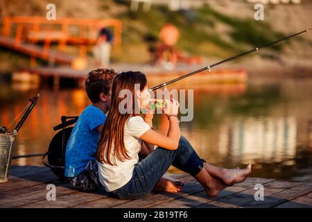 Zwei kleine kleine junge Freunde, Junge und Mädchen, die Sandwiches essen und an einem sonnigen Sommertag auf einem See angeln. Kinder spielen. Freundschaft. Stockfoto