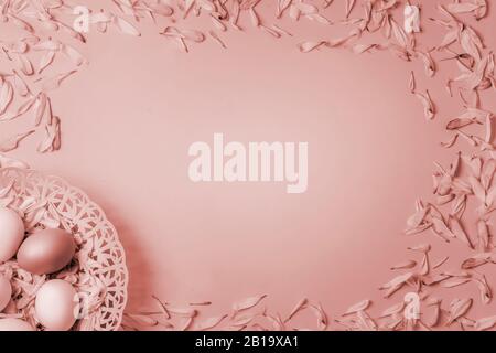 Ostereier in einem Korb und bunte Blütenblätter mit Frühlingsblumen aus Kamille und Chrysanthemum auf einem blassrosa roten matten Hintergrund. Kopierbereich. Mockup. Stockfoto