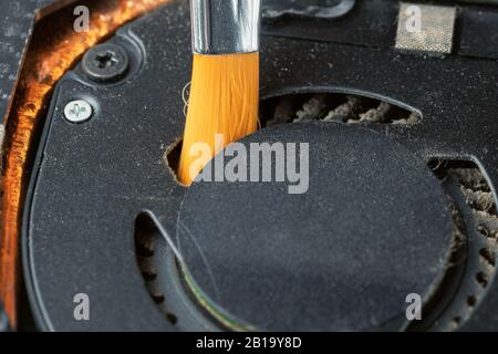 Reinigen eines schmutzigen, staubigen Notebook-Kühlsystems mit einer Bürste. Stockfoto