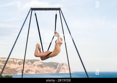 Fly-dance Gravity Yoga posiert in einer Hängematte mit Blick auf die Berge. Harmonie mit der Natur. Akrobatikturnen im Freien. Aktiver Frauensport. Stockfoto