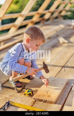 Kind (junge) Hammer Nägel mit einem Hammer in einer Holzplatte auf dem Dach Stockfoto