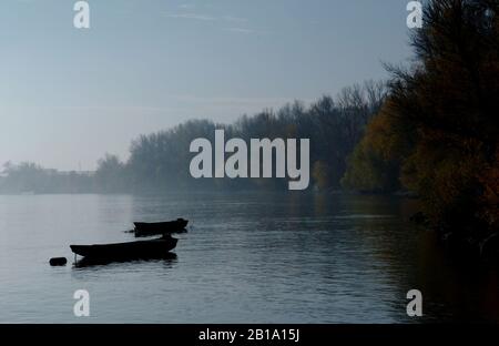 Kleine Fischerpaddelboote, die im Morgennebel am ruhigen Fluss verankert sind. Ruhige, schöne Landschaft im Herbst. Schönheit im Naturkonzept Stockfoto