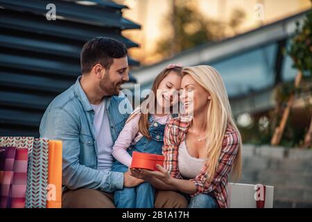 Glückliche Familie mit Einkaufstaschen.Familieneinkäufe.Junge Eltern und ihre Tochter tragen Einkaufstaschen.Fröhliche Familie mit Einkaufstaschen, die ausruhen Stockfoto