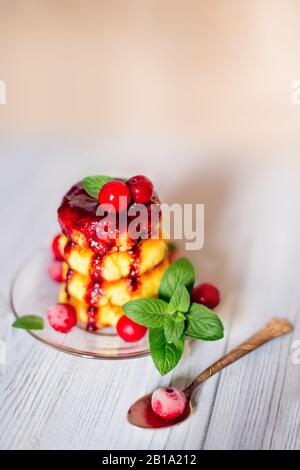 Käsekuchen mit Beerenmarmelade und Kirsche auf weißem Holztisch, Frühstück oder Mittagessen. Hausgemachte traditionelle ukrainische und russische Küche. Stockfoto