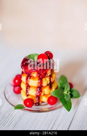 Käsekuchen mit Beerenmarmelade und Kirsche auf weißem Holztisch, Frühstück oder Mittagessen. Hausgemachte traditionelle ukrainische und russische Küche. Stockfoto