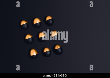 Neun schwarze und goldene Ostereier auf dunkelgrauem Grund. Flaches Layout, Draufsicht, Kopierbereich. Stockfoto