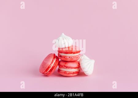 Rosafarbene Makronen und weiße Marshmallows auf pinkfarbenem Pastellhintergrund. Platz für Text. Stockfoto