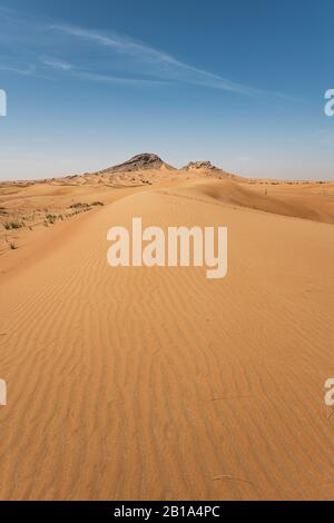 Vertikale Sanddünen-Landschaft mit Bergen im Hintergrund, blauem Himmel und großem Textraum Stockfoto