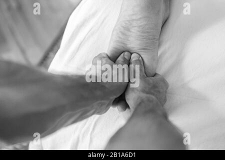 Professioneller Physiotherapeut massiert unerkennbare Mannfüße mit einem Druck. Schwarz-Weiß-Bild der Sportmassage. Ansicht von oben Stockfoto
