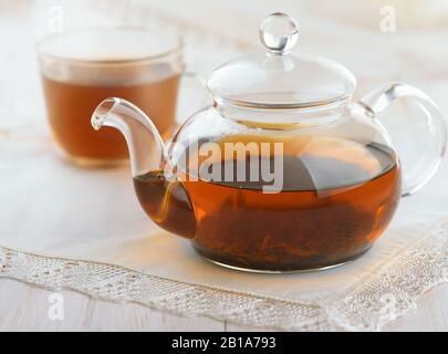 Glaskanne und Tasse mit frischem schwarzem Tee auf weißem Holztisch Stockfoto