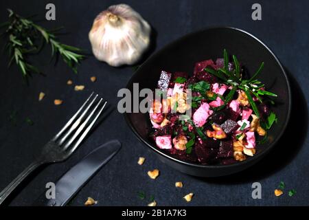 Rote-Bete-Salat mit Fetakäse und Walnüssen in einer braunen Keramikschale auf schwarzem Schiefer mit Petersilie Stockfoto