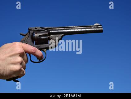 Mann, der einen Revolver im Kaliber .44 oder .45 im Freien mit blauem Himmel hält. Stockfoto