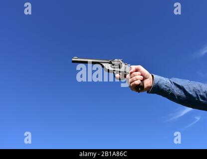 Mann, der einen Revolver im Kaliber .44 oder .45 im Freien mit blauem Himmel hält. Stockfoto