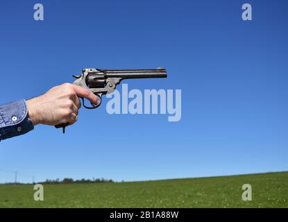 Mann, der einen Revolver im Kaliber .44 oder .45 im Freien mit blauem Himmel hält. Stockfoto