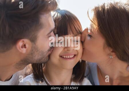 Nahaufnahme liebevoller Eltern küsst kleine Tochter auf Wangen Stockfoto