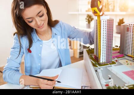 Fröhliche lächelnde Frau, die gern Stadtteilgestaltung oder große komplexe, nahe aufstellbare Fotos macht. Lieblingsjob, Beruf, Beruf, Schaffung eines einzigartigen Desigs Stockfoto