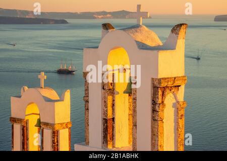 Griechenland. Sonnenuntergang auf der Insel Thira. Glocken der griechischen Kapelle in Oia und Hafenblick mit Segelbooten Stockfoto