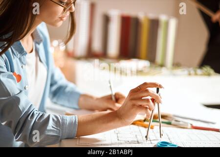 Junger, junger, schöner Architekt, der mit einem Paar Kompasse einen Kreis bildet. Nahaufnahme des Fotos mit Seitenansicht. Zugeschnittenes Foto Stockfoto