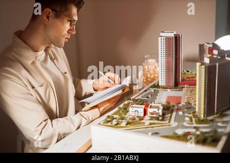 Junger Mann, der Details zum Bau schreibt, Mann, der mit Dokumentation arbeitet, Papierarbeit. Nahansicht Foto, Kerl, der seine Beobachtungen schreibt, empfehlen Stockfoto