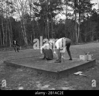 Golf spielen: Afrikanisch-amerikanischer Caddy und Golfer der weißen Frau erstellen ein Wet-Sand-T-Shirt auf dem T-Stück, c 1910. In diesen Jahren gab es keine einfachen Holz-Tees. Golfer machten einen kleinen Hügel mit nassem Sand und legten den Ball darauf. Sehen Sie die Wasserdose und den Sandkasten auf der rechten Seite. Die quadratische, erhöhte Oberfläche wurde als "Abzweigboden" oder "Abzweigkasten" bezeichnet. Frühe T-Stücke waren erfunden worden, aber die meisten Golfspieler verwendeten sie erst in den 1920er Jahren. Um meine anderen, Golf-bezogenen Vintage-Bilder zu sehen, suchen Sie: Prestor Vintage Golfsport Afrikaner Stockfoto