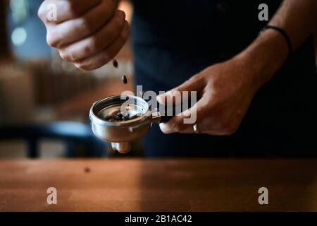 Mann, der Kaffeebohnen in den Portafilter wirft, Nahaufnahme der Seitenansicht Stockfoto