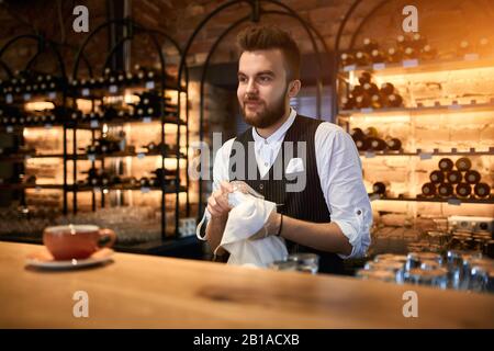 Hübsche bärtige Barkeeper wischen ein Glas. Nahaufnahme Foto, stilvolles Barmen Trocknen eines Glases mit einem Küchentuch Stockfoto