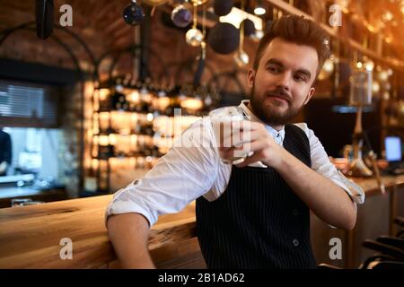 Entspannter, fröhlicher bärtiger Kellner, der eine Kaffeepause am Arbeitsplatz hat, Nahaufnahme. Kerl genießt das Trinken leckerer Cupuchino. Nahaufnahme Stockfoto