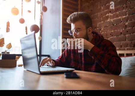 Junger attraktiver bärtiger Mann, der Computerspiele spielt, Tee im Café trinkt. Nahansicht Foto.Kaffeeliebhaber Stockfoto