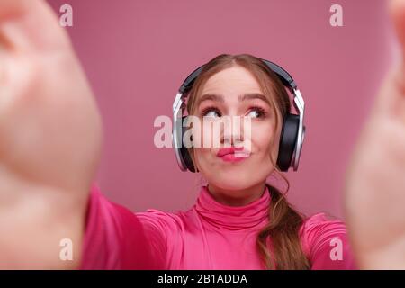 Nahaufnahme des Porträts der nachdenklichen jungen Rotkopffrau, die selfie mit zwei Händen macht. Lustige lächelnde Mädchen mit Kopfhörern, die ein Geschenk auf Stift isoliert haben Stockfoto