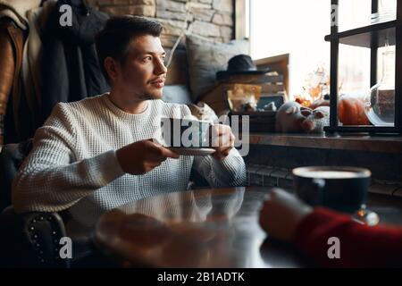 Nachdenklicher Mann, der über seine Liebe nachdenkt, Freundin, während er auf das Fenster blickt. Nahansicht Foto, Kerl genießt Cappuccino allein zu trinken Stockfoto