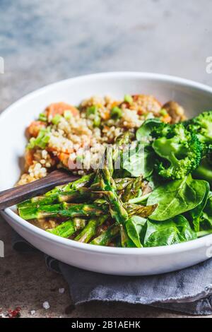 Vegane Mittagsschüssel mit Quinoa, Brokkoli, Spargel und Pilzsauce in einer weißen Schüssel. Stockfoto