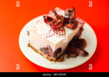 Japanische Käsekuchen mit Kirschsauce und frischen Kirschen auf der Keramikplatte und rotem Hintergrund, süßes Dessert Stockfoto