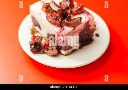 Japanische Käsekuchen mit Kirschsauce und frischen Kirschen auf der Keramikplatte und rotem Hintergrund, süßes Dessert Stockfoto