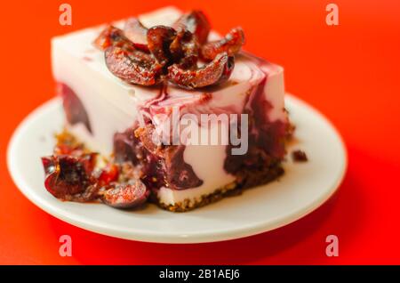 Japanische Käsekuchen mit Kirschsauce und frischen Kirschen auf der Keramikplatte und rotem Hintergrund, süßes Dessert Stockfoto