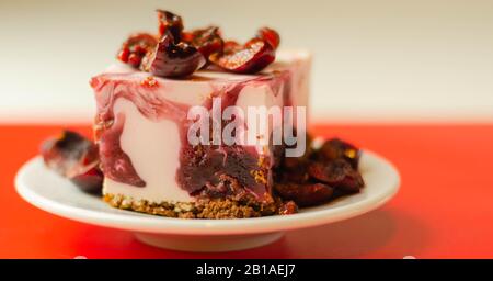 Japanische Käsekuchen mit Kirschsauce und frischen Kirschen auf der Keramikplatte und rotem Hintergrund, süßes Dessert Stockfoto