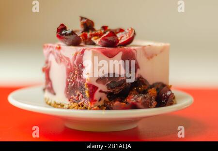 Japanische Käsekuchen mit Kirschsauce und frischen Kirschen auf der Keramikplatte und rotem Hintergrund, süßes Dessert Stockfoto