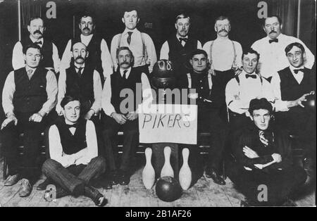 Bowling Team, The "Pikers" im Jahr 1908, in Milwaukee, Wis. Das sind 14 Männer um drei Pins, ihr Teamname und das Bowler-Ende der Ball-Rückkehr. Auf dem Foto sind 3 Bowlingbälle zu sehen. Männer sind alle schwarz-weiß gekleidet, manche mit Hosenträgern. Viele Schnurrbart auf ernsthaften Gesichtern. Um meine anderen, sportbezogenen Vintage-Bilder zu sehen, suchen Sie: Prestor Vintage-Sport Stockfoto