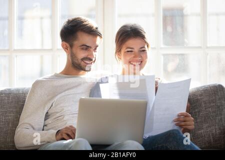 Lächelnde Paare halten Papierkram, die Rechnungen online bezahlen Stockfoto