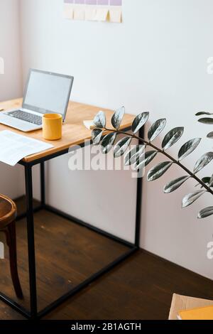 Freiberufler mit Laptop, Becher auf Holztisch. Nahaufnahme Foto.vertikale Aufnahme. Leerer Raum mit modernem Interieur. Stockfoto