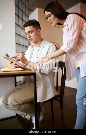 Junge fröhliche Paare unterzeichnen Dokumente.Familie konzentriert sich auf die Arbeit mit Papier. Nahansicht Foto, Frau unterstützt ihren Mann bei der Aufarbeitung Stockfoto