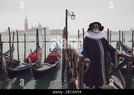 Ein Mann in Tracht beim Karneval in Venedig neben Gondeln und mit der Kirche San Giorgio Maggiore im Hintergrund Stockfoto