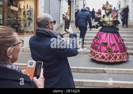 Ein in Tracht gekleideter Karnevalsgör posiert für Touristen in Venedig Stockfoto