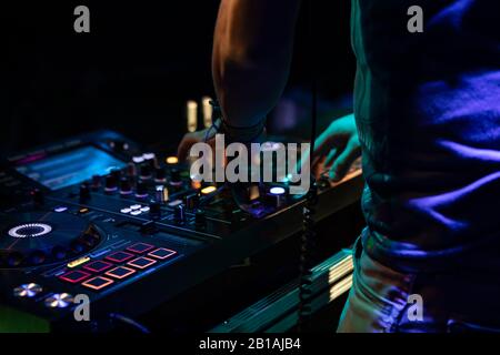 Eine Nahaufnahme der Atmosphäre mit selektivem Fokus auf die Hände eines Musik-DJ, der ein EDM-Set spielt, mit Mischpult und bunter Bühnenbeleuchtung bei Nacht Stockfoto