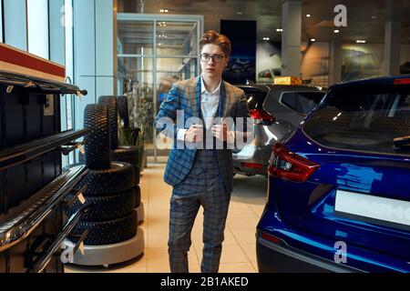 Perfektes Auto für mich. Junger gutaussehender Mann, der seine Jacke in grau kariertem Anzug in der Nähe des Autos im Autohaus knallt, Nahaufnahme Stockfoto