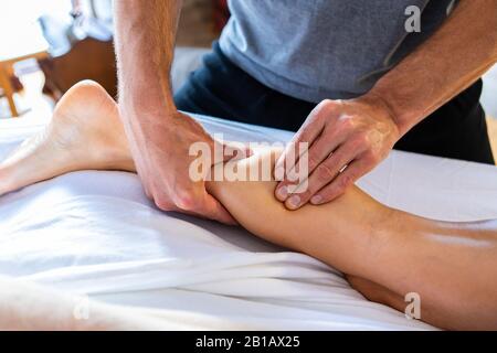 Junge, erfahrene Masseurin bei therapeutischer Massage. Masseur arbeitet. Spa-Massage in gemütlicher häuslicher Umgebung. Massagetherapie mit Ölbeinen Stockfoto