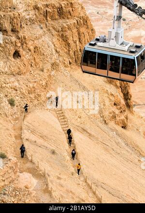 Die Seilbahn steigt von der Spitze Masadas ab, während die Menschen unter ihr hinuntergehen. Stockfoto