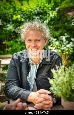 Blonder junger Mann, der mit einem selbstbewussten Lächeln in die Kamera blickt Stockfoto