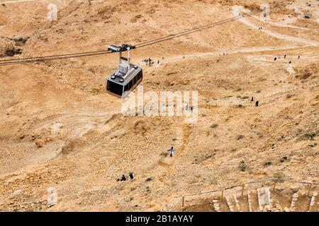 Die Seilbahn im Masada-Nationalpark im Süden Israels steigt von oben herab, wenn die Menschen darunter spazieren. Stockfoto