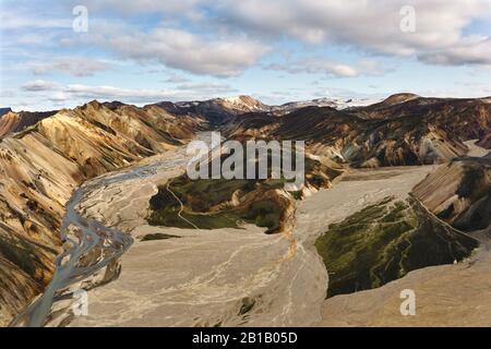 Herrlicher Luftblick auf das trockene Flussbett und den rauen Bergrücken gegen den bewölkten Himmel im isländischen Hochland Stockfoto