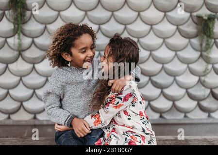 Nette Geschwister lächeln und lachen einander an, während Umarmung draußen Stockfoto